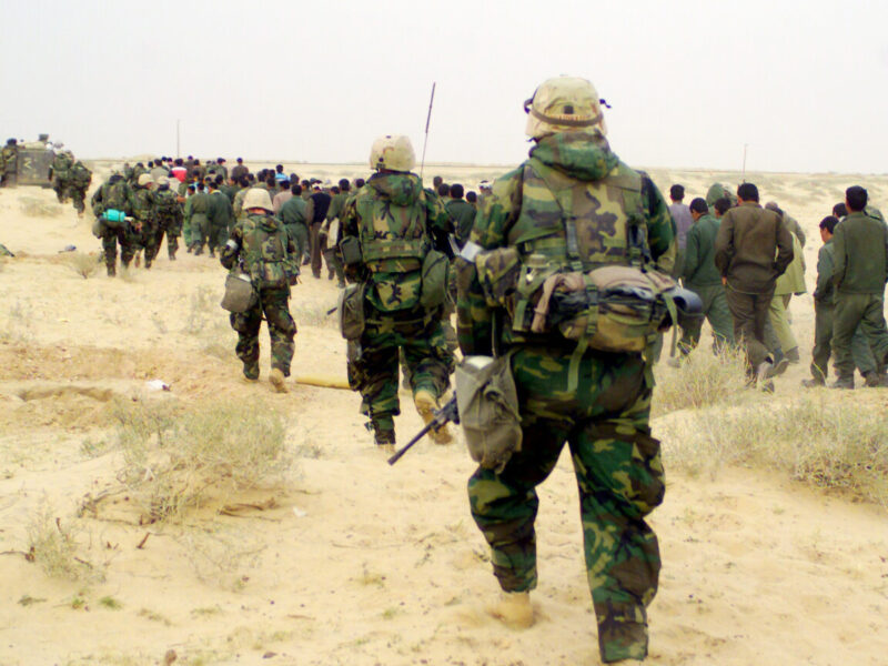 A photo of U.S. Marines escorting captured enemy prisoners to a holding area in the desert of Iraq on March 21, 2003.