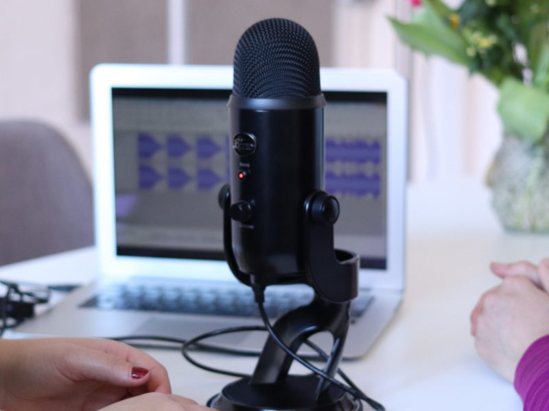 An image of a podcast microphone on a white table in front of a laptop.