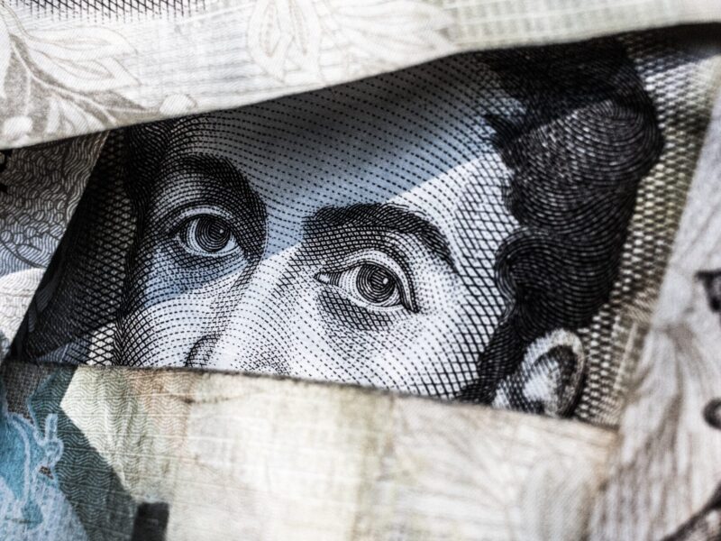 An image of a pile of bills. The eyes of one of a person on one of the bills is in focus in the centre of the image.