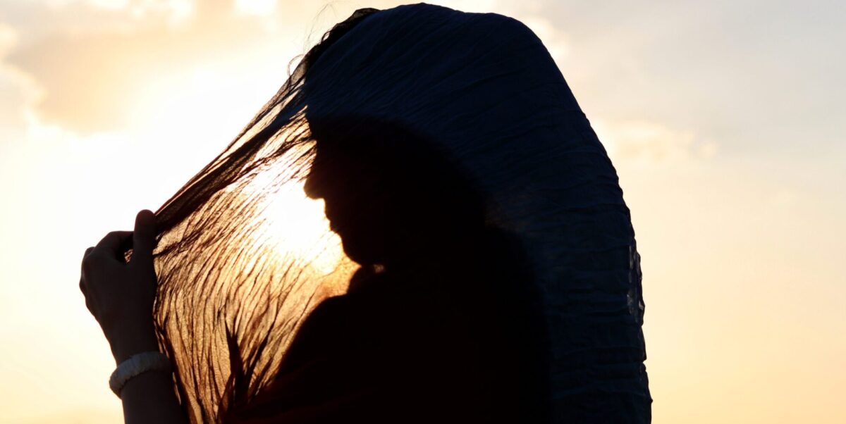 A woman wearing a hijab, a sunset in the background.