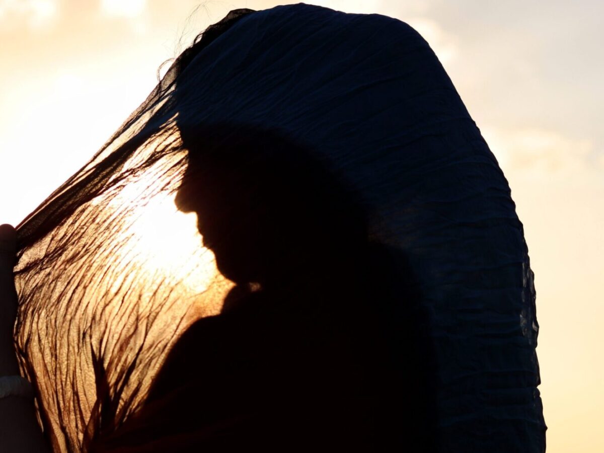 A woman wearing a hijab, a sunset in the background.