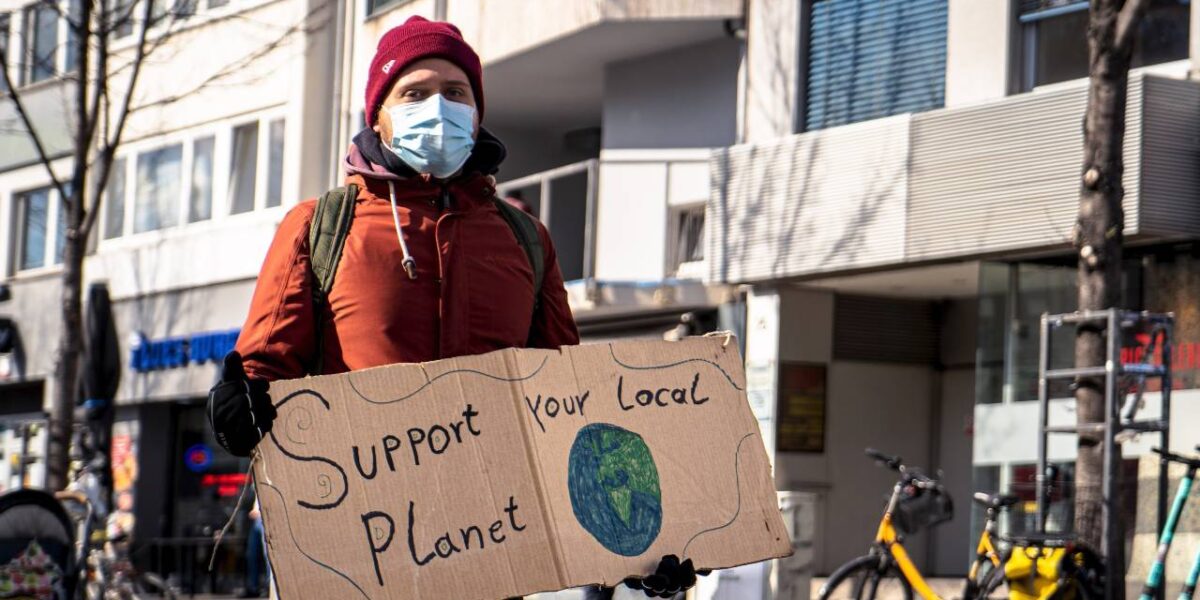 A climate protester holding a sign saying "Support your local planet."