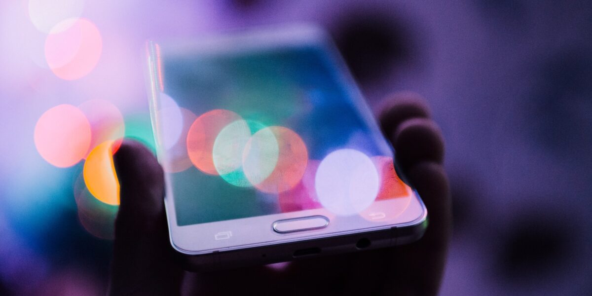 A photo of a hand holding a smartphone, source of both news and social media.