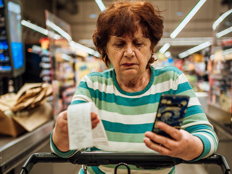 An image of a woman looking at a receipt and her phone while in a grocery store.