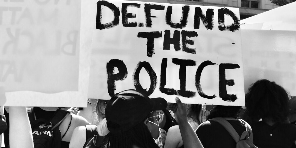 A person holds a sign reading "defund the police" at a protest.