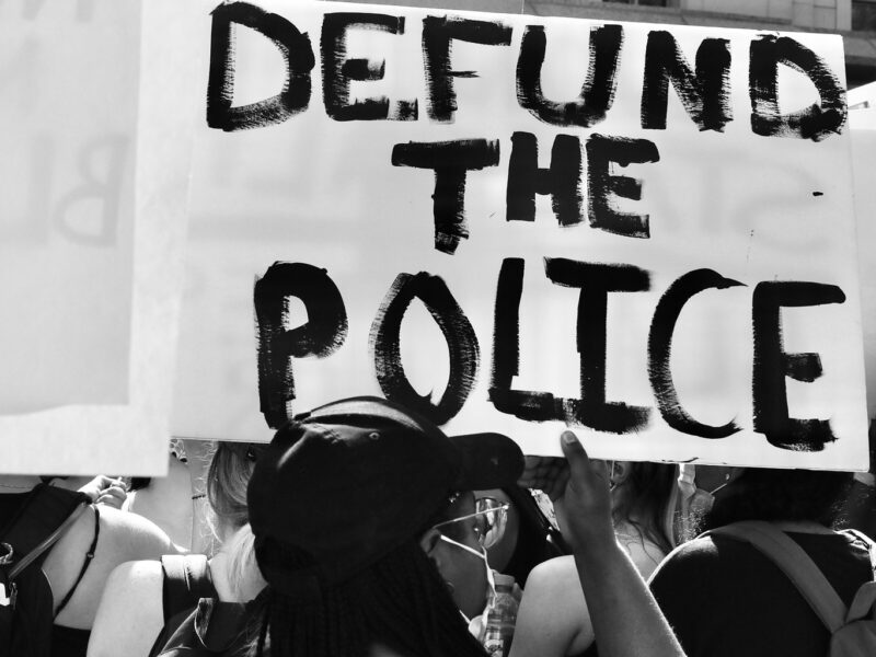 A person holds a sign reading "defund the police" at a protest.