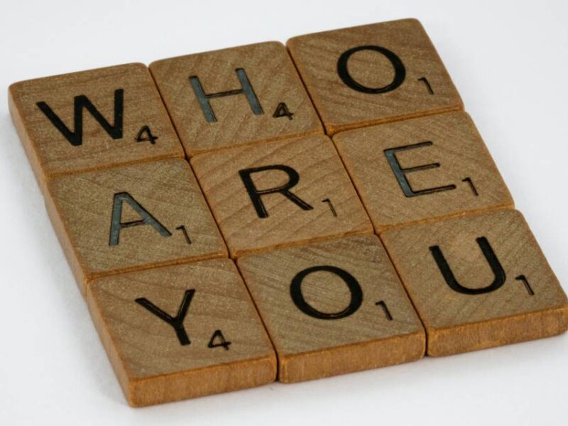 Nine square pieces from the game Scrabble spelling out the phrase "who are you?"