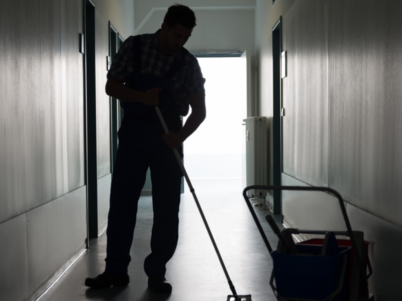 A single custodial worker mops in a dimly lit hallway.