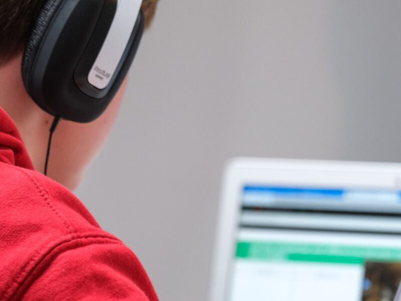 An over-the-shoulder picture of a student with headphones looking at a computer screen.