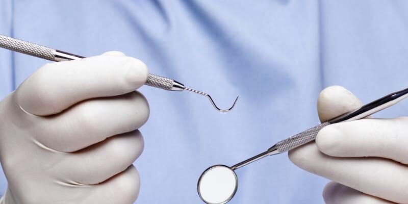 A close-up image of gloved hands holding dental tools.