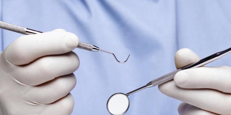 A close-up image of gloved hands holding dental tools.