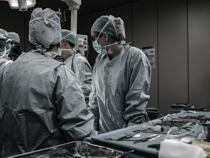 A group of surgeons standing next to a table of unused surgical tools, looking at something out of frame to the left.