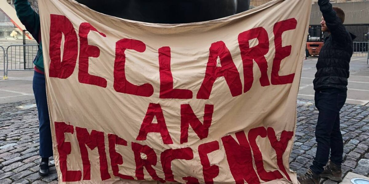 Two people holding a banner with the words "declare and emergency" painted in red.