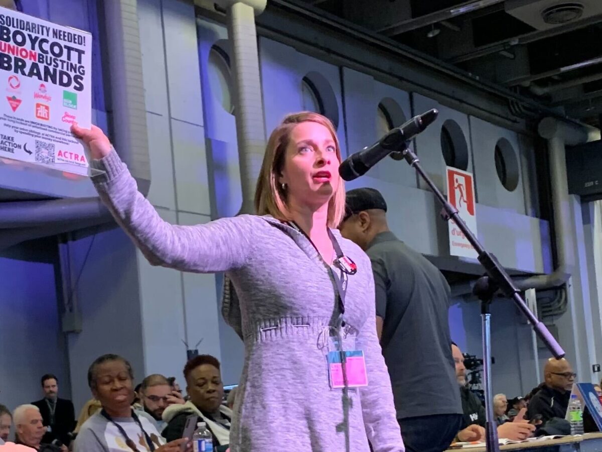 Eleanor Noble, National President of ACTRA stands in front of a microphone holding up a poster calling for boycotts of Canadian brand names that are locking out her members.