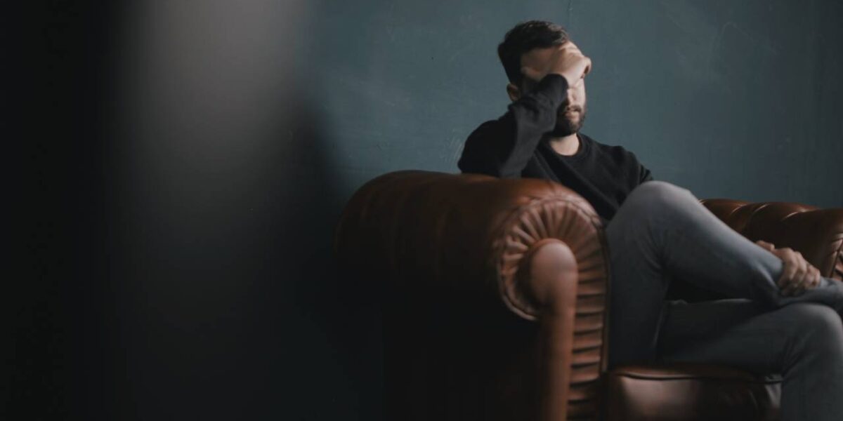 A man sitting on a couch with a hand covering his face.