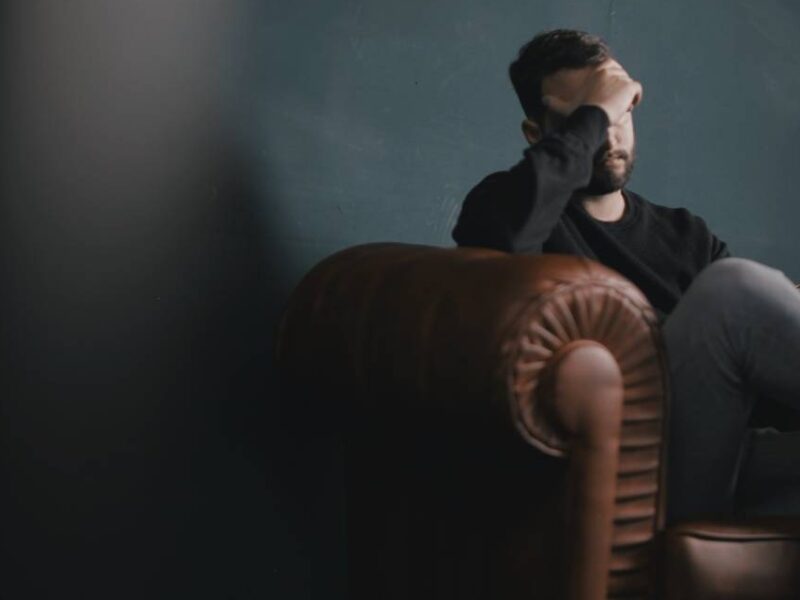 A man sitting on a couch with a hand covering his face.