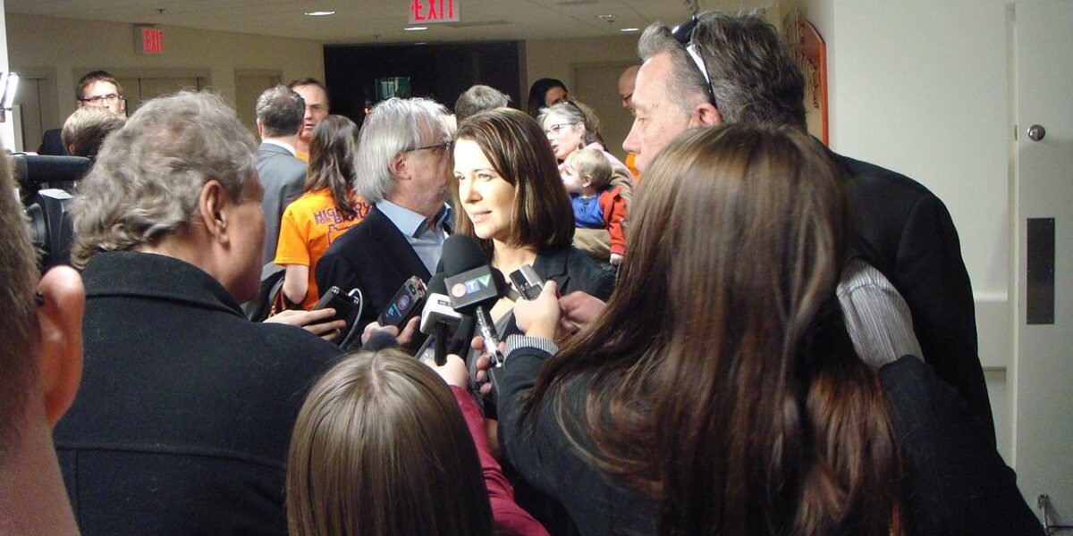 Danielle Smith is surrounded by journalists from mainstream media, in a media scrum.