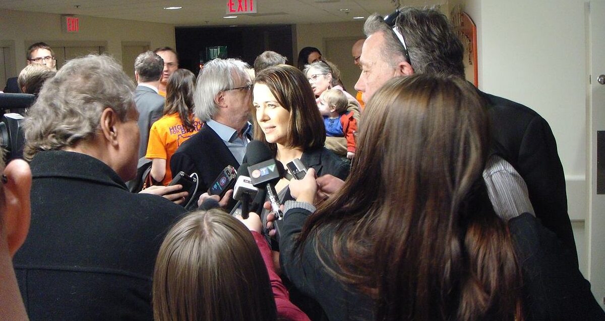 Danielle Smith is surrounded by journalists from mainstream media, in a media scrum.