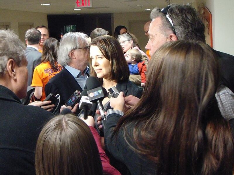 Danielle Smith is surrounded by journalists from mainstream media, in a media scrum.