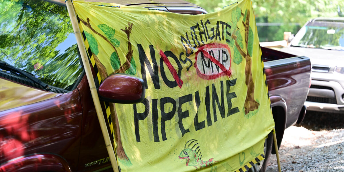 A sign expressing opposition to the Mountain Valley Pipeline leans against the side of a car.