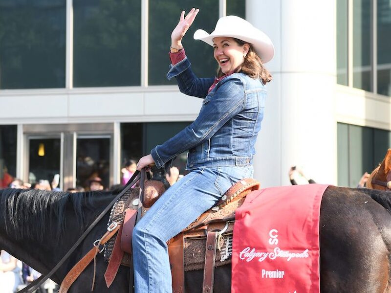 Photo of Alberta Premier Danielle Smith wearing cowboy gear, riding on horse