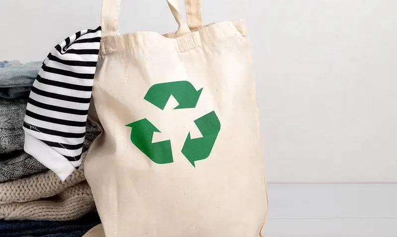 An image of clothes in a bag bearing the recycling symbol. Reusing or recycling clothing is a key part of sustainable fashion.