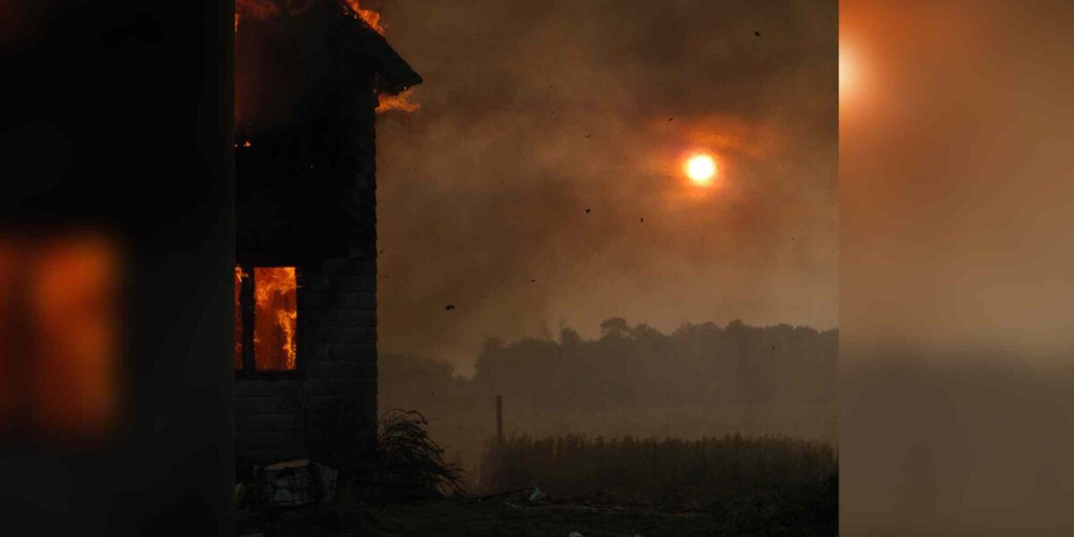 A house burns as smoke obscures the sun.