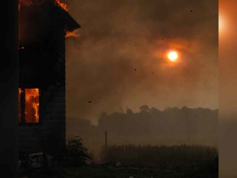 A house burns as smoke obscures the sun.