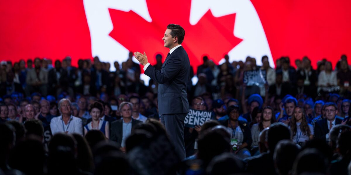 Pierre Poilievre at the 2023 Conservative Party convention with a large Canadian flag in the background.