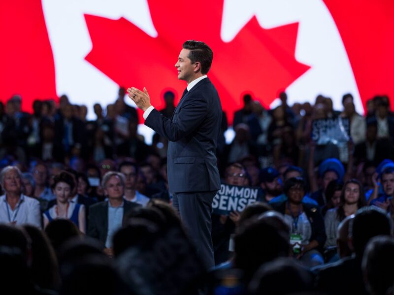 Pierre Poilievre at the 2023 Conservative Party convention with a large Canadian flag in the background.