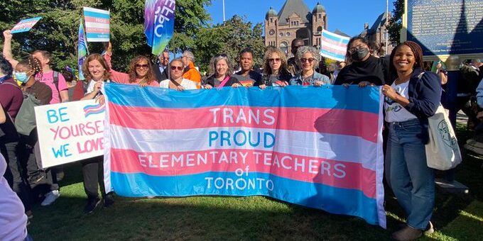 Teachers holding a flag that says "trans proud elementary teachers of Toronto."