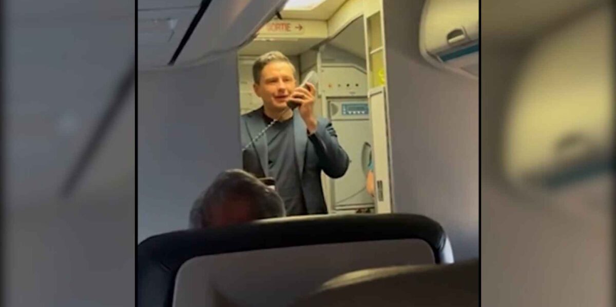 Pierre Poilievre standing at the front of a plane cabin holding the microphone of the plane's public address system.