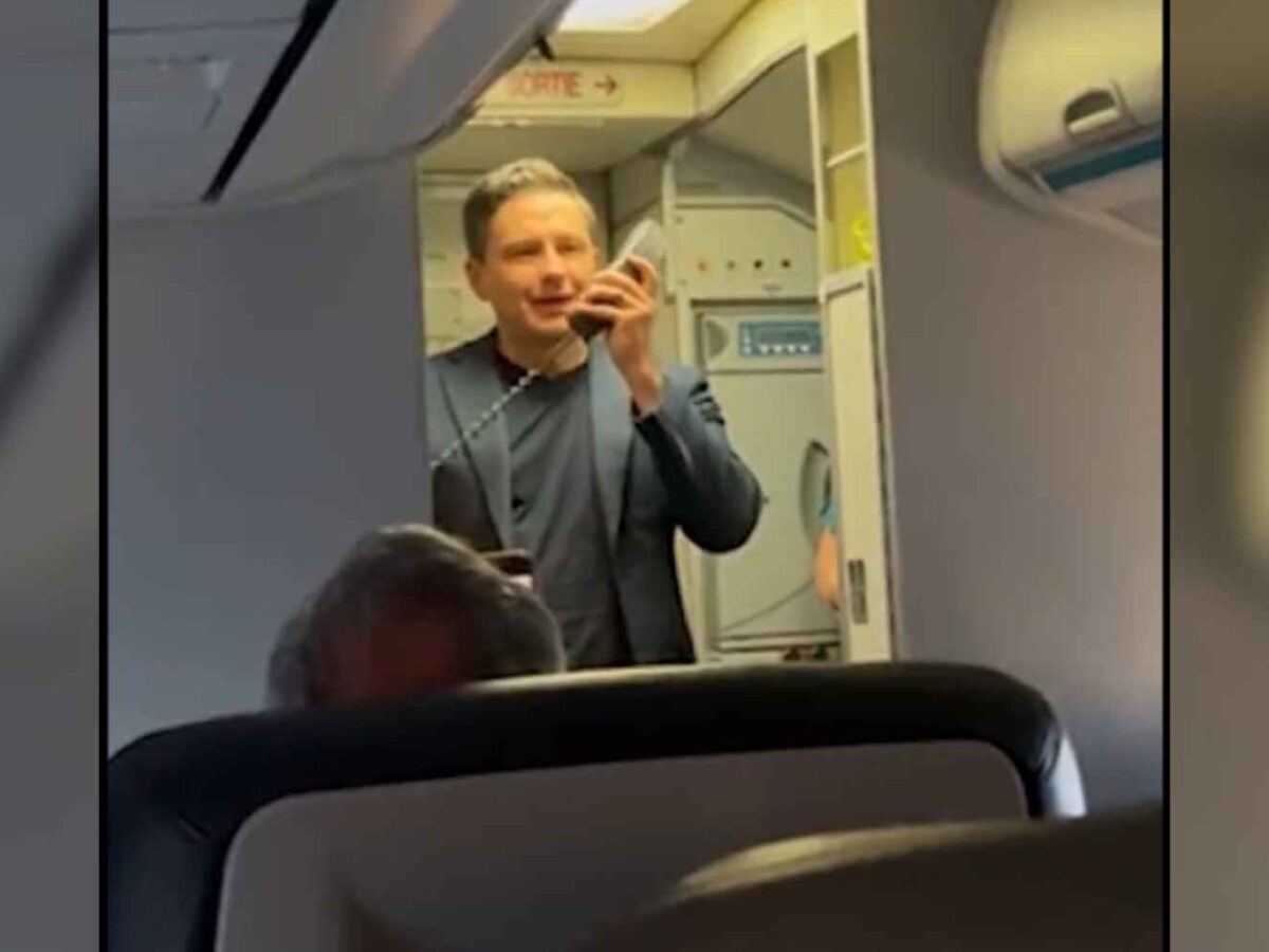 Pierre Poilievre standing at the front of a plane cabin holding the microphone of the plane's public address system.