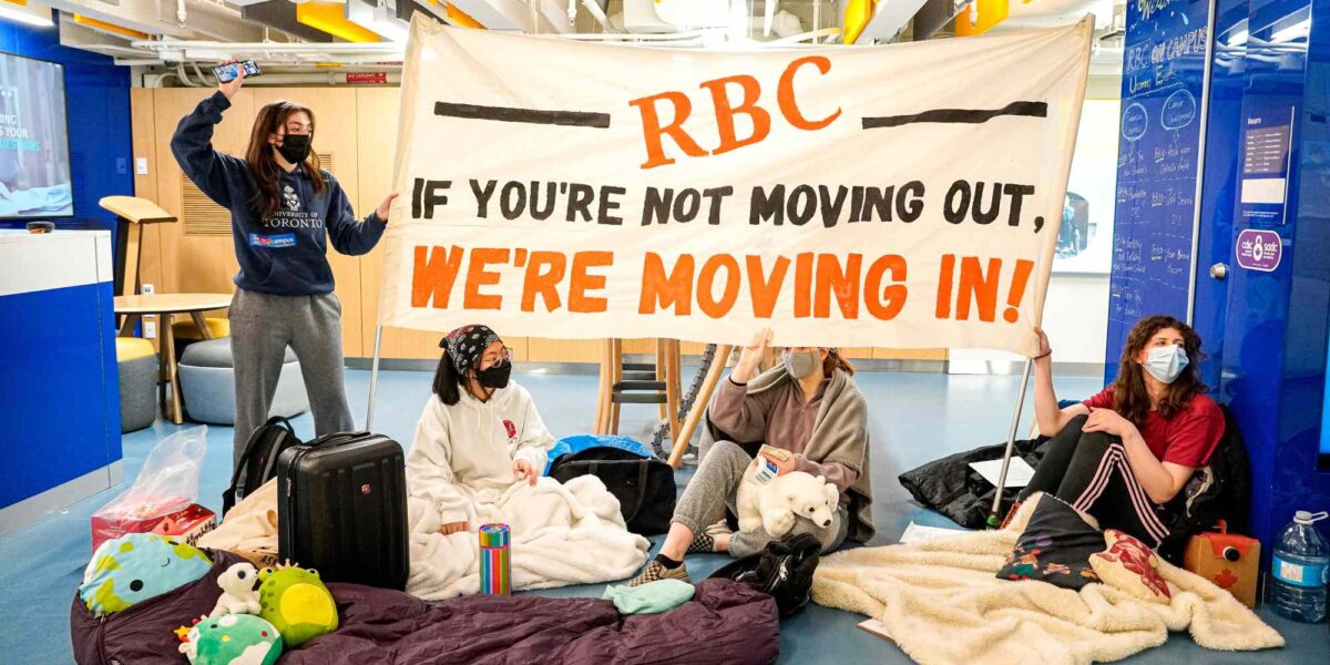 Students at the University of Toronto engaging in a climate protest against RBC. They hold a sign saying "RBC: If you're not moving out, we're moving in!"