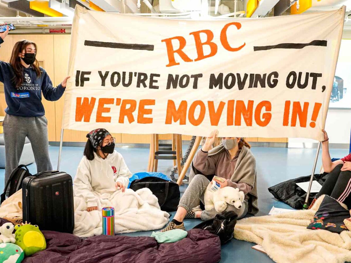 Students at the University of Toronto engaging in a climate protest against RBC. They hold a sign saying "RBC: If you're not moving out, we're moving in!"