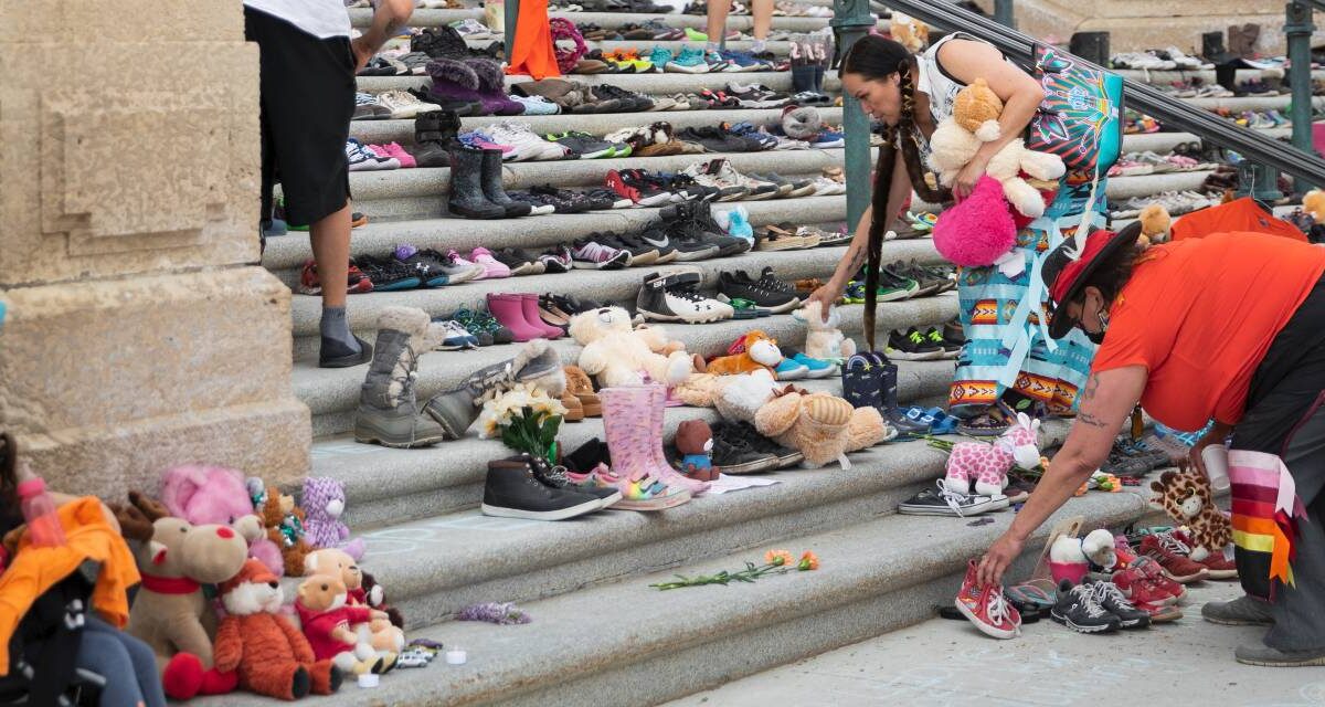 Indigenous women placing stuffed animals on the steps of a government building in Regina, Saskatchewan.