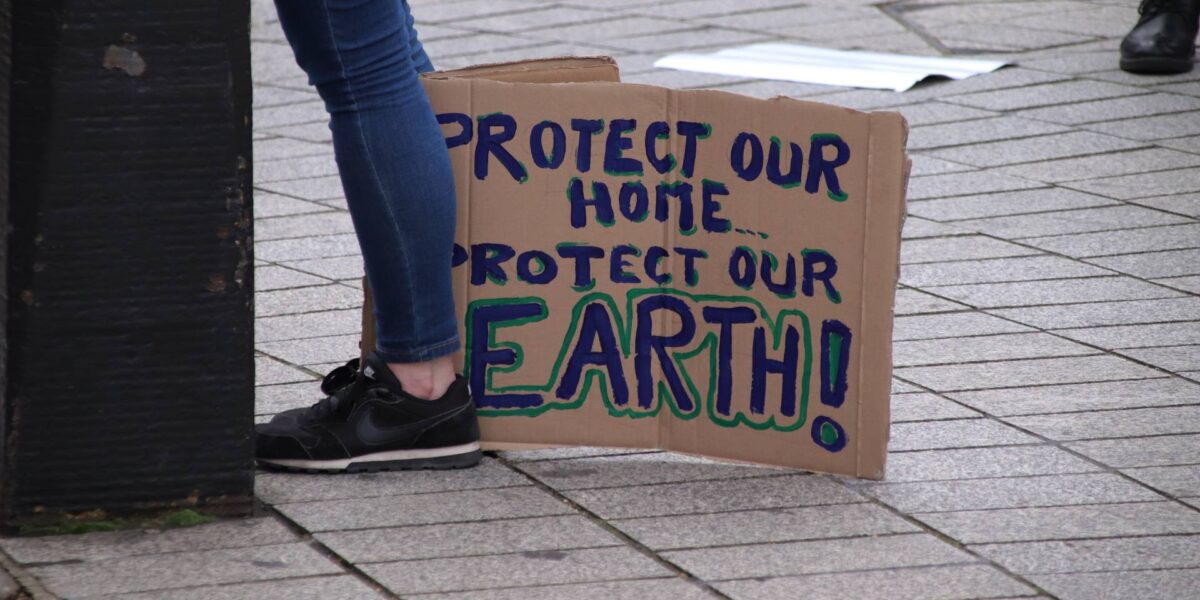 A climate strike sign reads "Protect our home, protect our Earth."