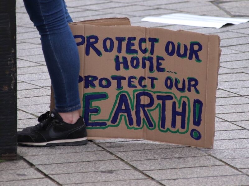 A climate strike sign reads "Protect our home, protect our Earth."