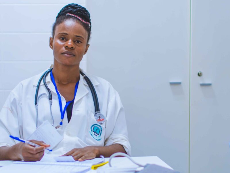 An image of a medical professional looking into the camera with papers strewn about the desk in from of her