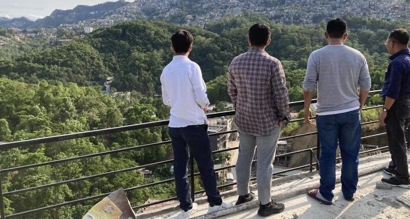 An image of a group of media and news workers on a mountain, looking onto the valley.