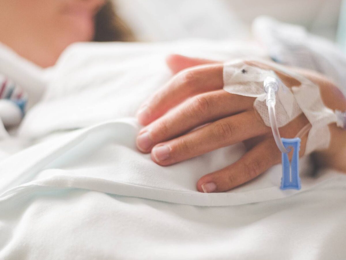 A person receiving hospital care lying on a bed with an intravenous tube in their hand.