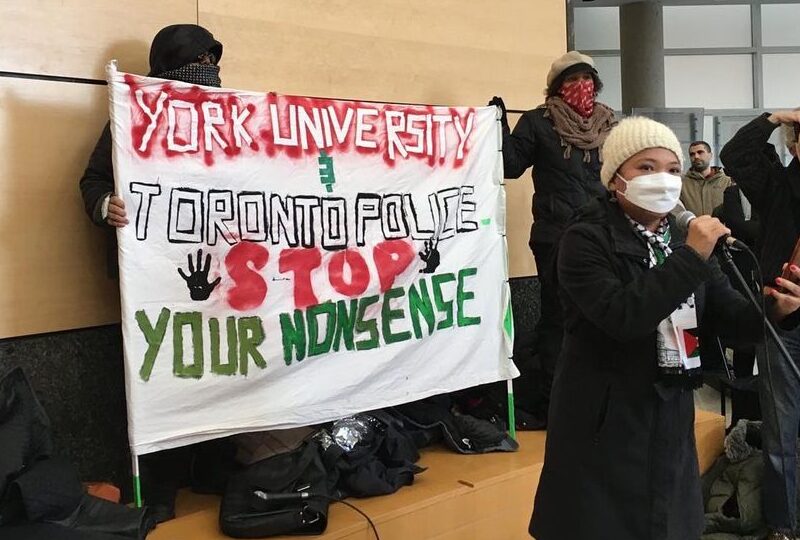York University students speaking at Tuesday’s walkout. A student speaks at a microphone while another in the background holds up a sign that reads: "York University, Toronto Police, stop your nonsense."