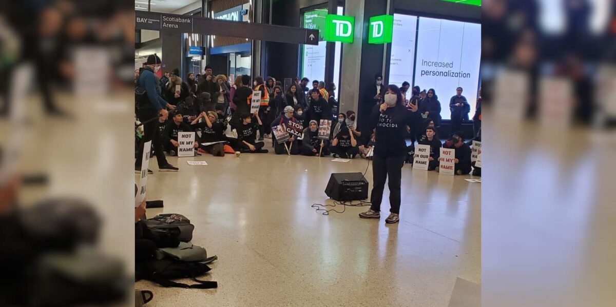 A woman speaks on a microphone at a Not in my name protest in Toronto.