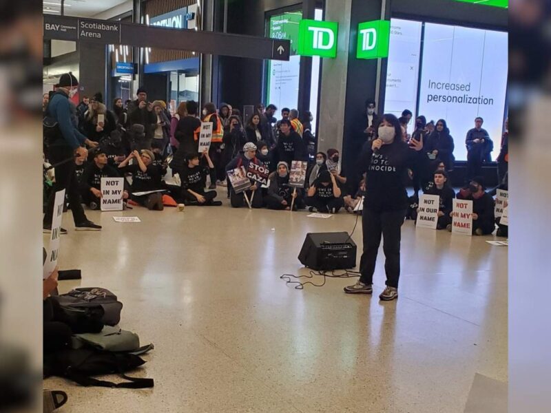 A woman speaks on a microphone at a Not in my name protest in Toronto.