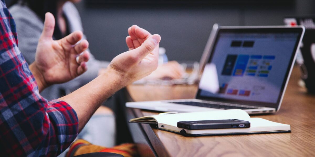 A person gesturing with their hands at a boardroom table.