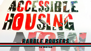 A sign reading: Accessible Housing Now! And the rabble rousers logo.