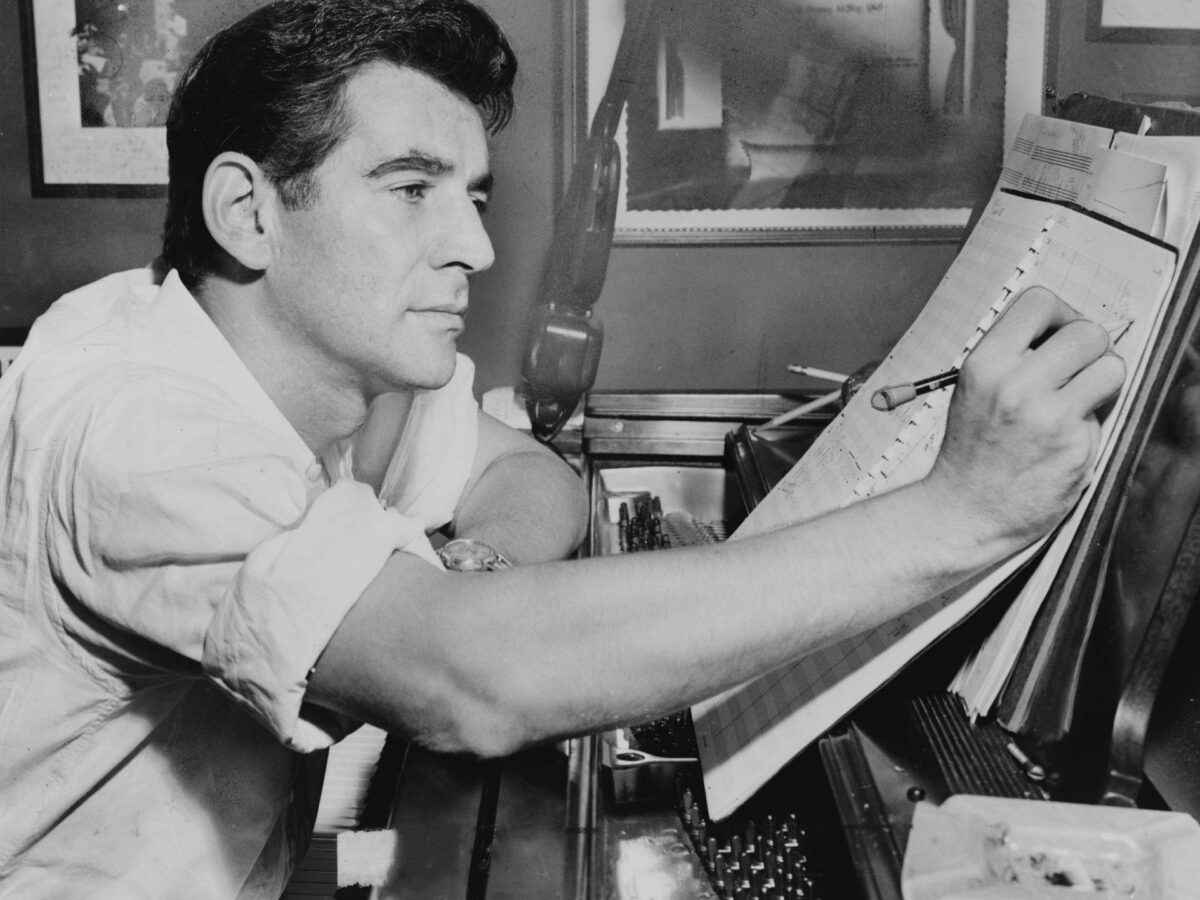 Leonard Bernstein seated at piano, making annotations to musical score.