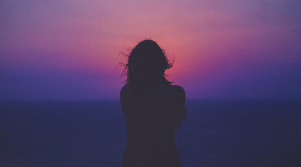 A woman facing a sunset.