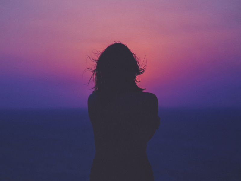 A woman facing a sunset.