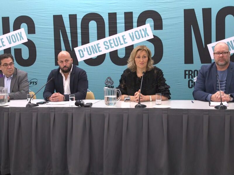 Four leaders of the Front commun sit at a table during a press conference.